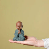 Petite statue moine bouddhiste salutation sur main d'homme avec fond vert kaosix