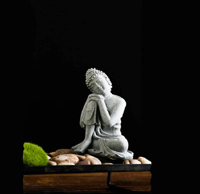 Statue Bouddha assis penseur posé sur des galets de pierre avec fond noir Kaosix