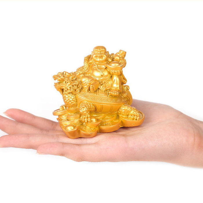 Statue bouddha rieur sur tortue dragon couleur doré posée sur la peaume d'une main et un fond blanc Kaosix