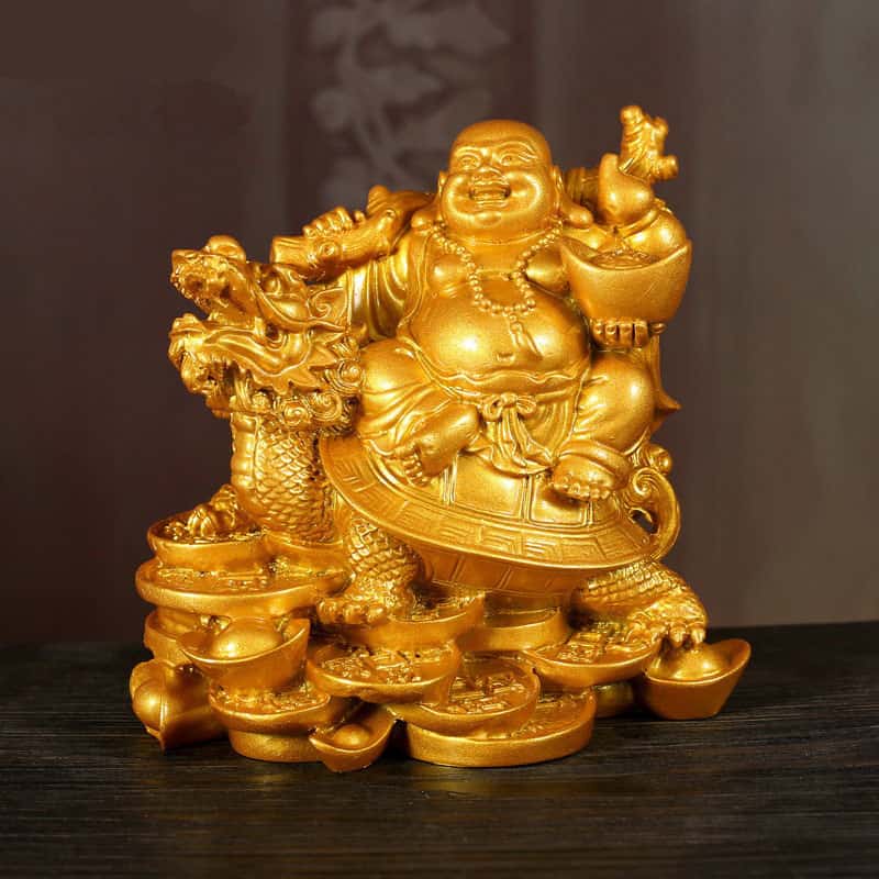 Statue bouddha rieur sur tortue dragon couleur doré posée sur table en bois et fond marron Kaosix
