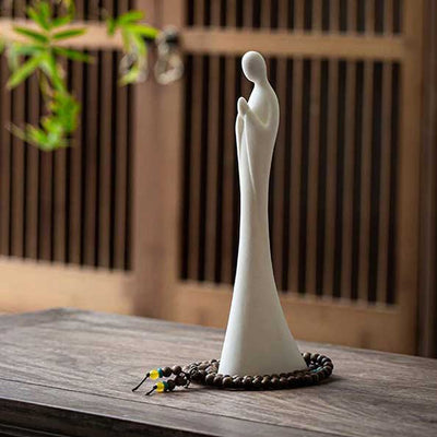Statue moine debout blanc Namaste sur une table en bois avec porte en bois en fond Kaosix