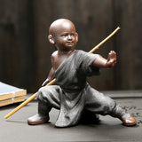 Statuette bouddhiste moine Shaolin bâton couleur gris debout sur un rocher et sur un fond noir Kaosix