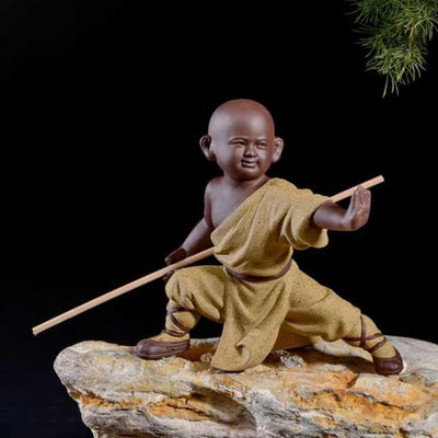 Statuette bouddhiste moine Shaolin bâton couleur jaune debout sur un rocher et sur un fond noir Kaosix