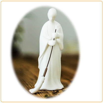 Statuette moine bouddhiste avec un balai vue de face sur une table en bois sur fond blanc et cadre orange Kaosix