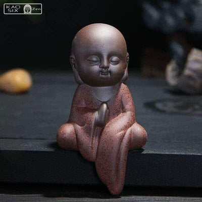 Statuette moine bouddhiste prière liberation robe rouge assis sur un rebord de table kaosix
