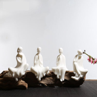 quatre statues moines bouddhistes zen en céramique blanche assis sur banc en bois avec fond gris Kaosix